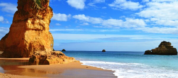 Praia dos Tres Castelos mit ockerfarbenen Felsen und goldgelbem Sandstrand in Portugal