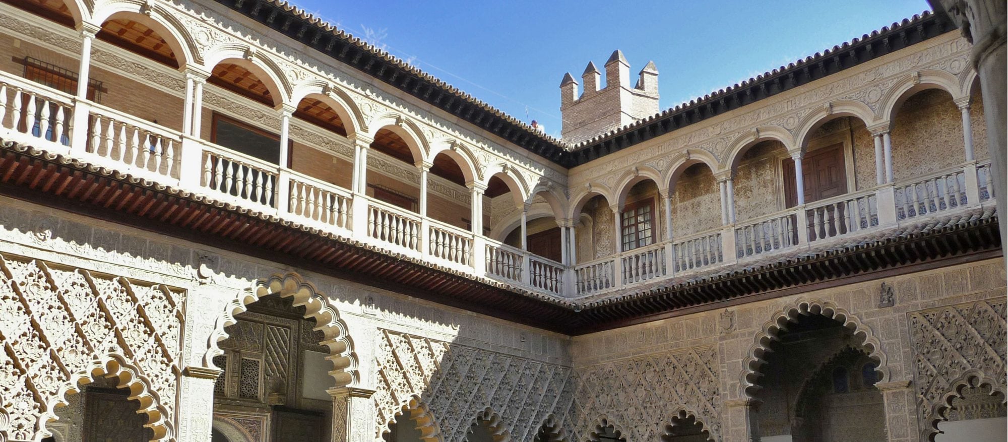 Blick in den Innenhof des Real Alcázar von Sevilla mit kunstvollen maurischen Bögen, Mosaiken und Palmen – UNESCO-Welterbe und königliche Residenz