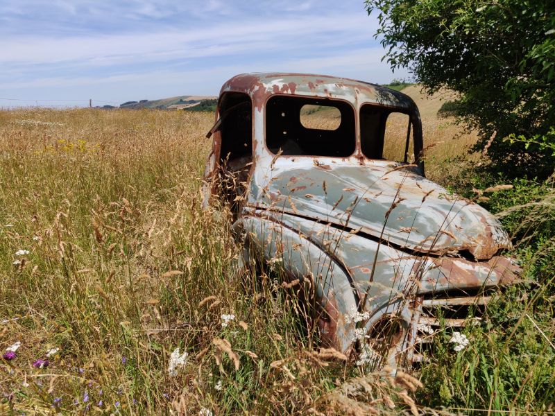 Auf einer Wiese mitten in der Landschaft rostet ein alter Citroën vor sich hin.