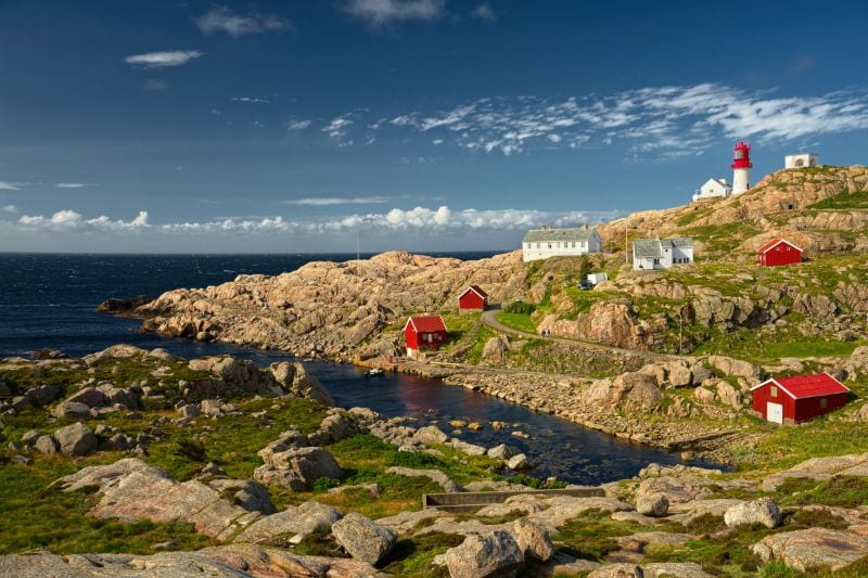 Felsiger Küstenabschnitt in der Nähe von Lindesnes; Leuchtturm Lindesnes fyr im Hintergrund