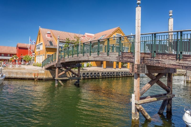 Eine Brücke über den Kanälen Kristiansands mit farbigen Holzhäusern im Hintergrund.