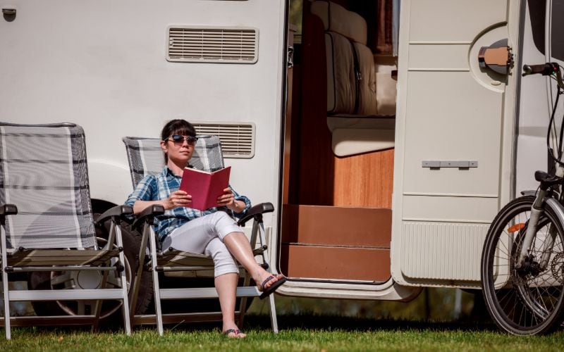 Frau mit Buch vorm Wohnmobil