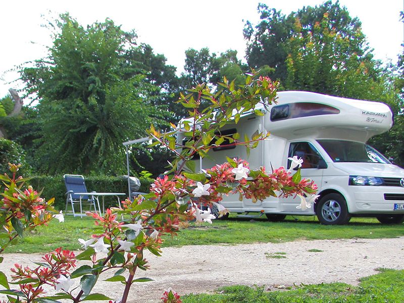 Camping La Poterie: Wohnmobil mit Klappstühlen und Tisch. Äste mit rosa und weißen Blüten im Vordergrund.