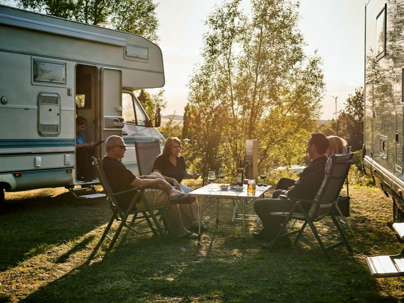 Gruppe Erwachsener, die mit alkoholischen Getränken vor Ihren Wohnmobilien auf dem Adults only- Campingplatz sitzen