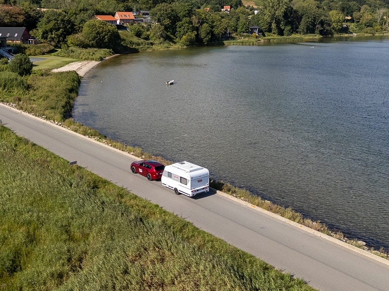Fahrendes Zugfahrzeug mit Caravan mit Fjord im Hintergrund