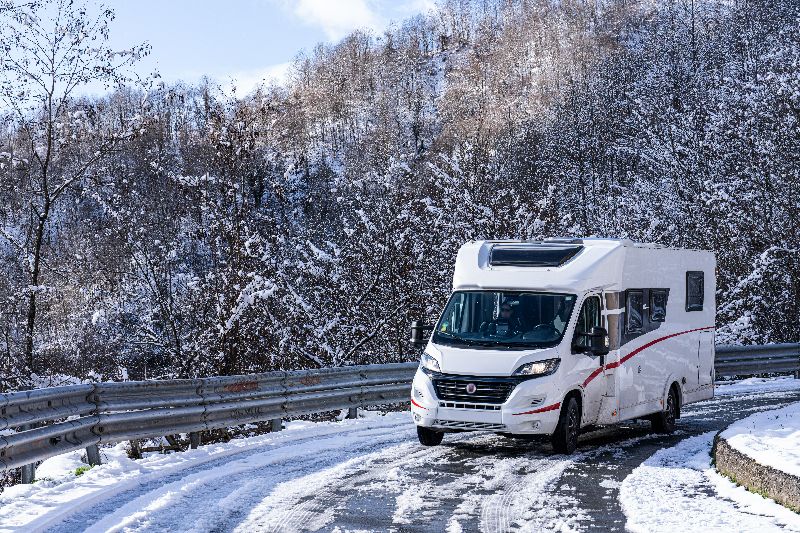 Wohnmobil auf verschneiter Bergstraße in Italien im Winter, unterwegs in alpiner Region mit eingeschränkter Zufahrt