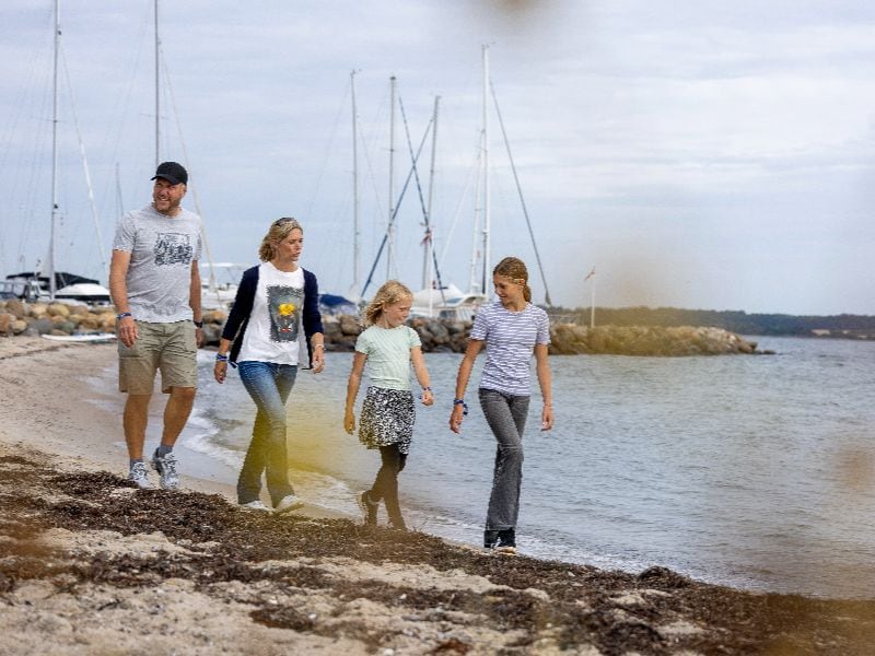 Petra, Jens, Leonie und Miriram spazieren entlang des Strandes im Hintergrund Segelboote