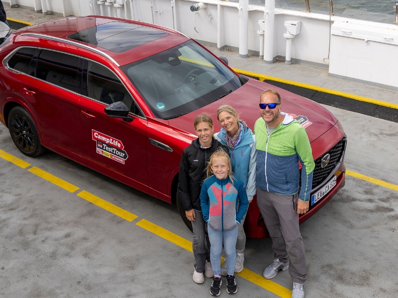 Die Rienhoffs stehen auf einer Fähre vor dem roten Mazda CX-80 