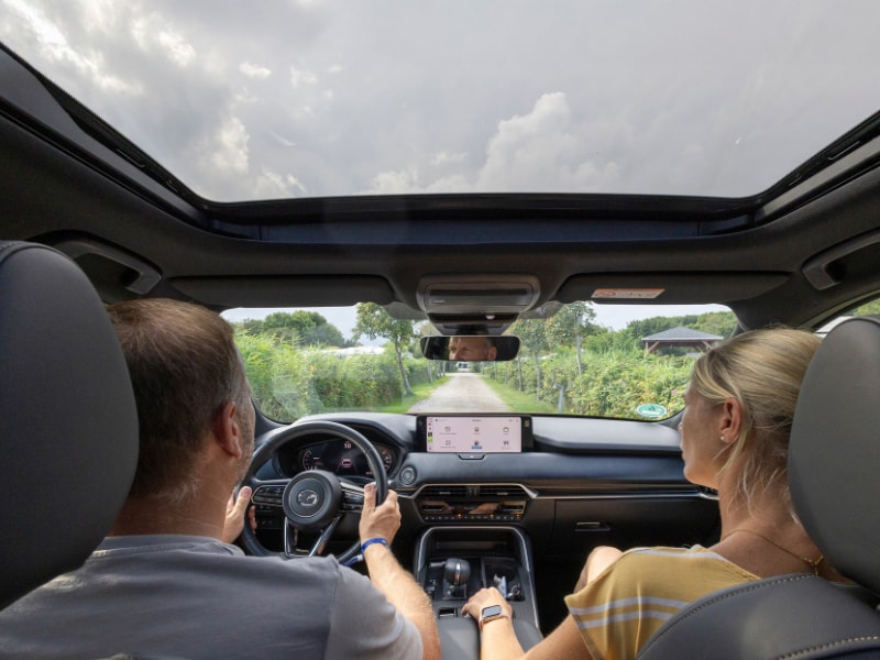 Jens und Petra sitzen im Mazda CX-80 und fahren über den Campingplatz