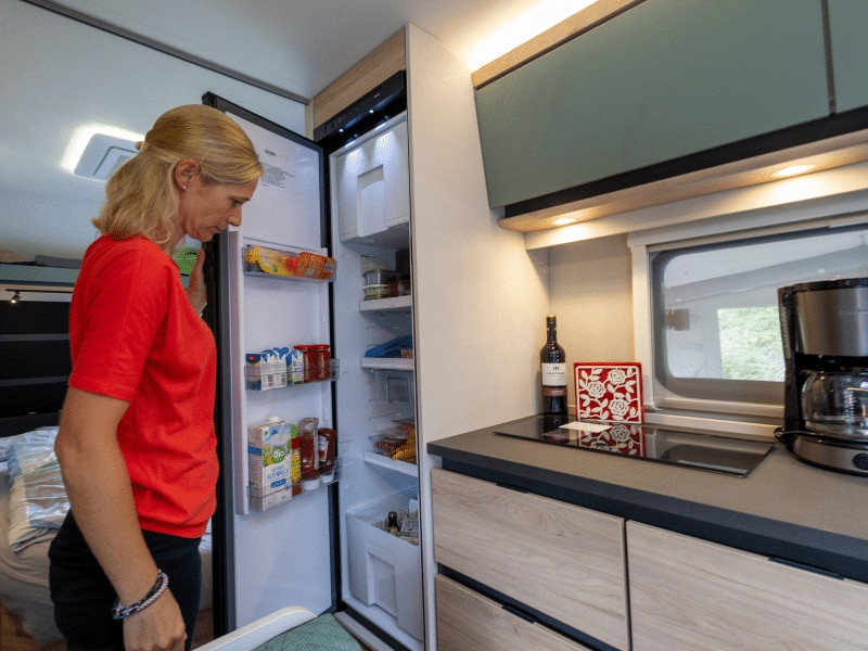Petra öffnet den Kühlschrank im Wohnwagen