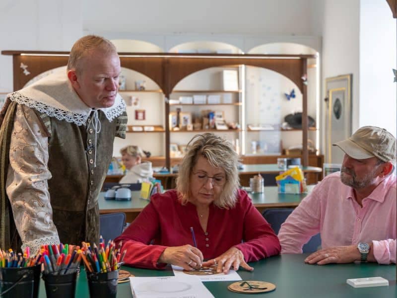 Herta zeichnet unter dem wachsamen Blick von Rasmus und Frank ein Motiv auf einen Teller.