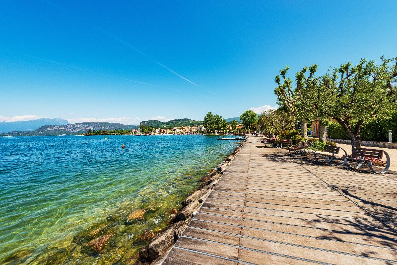Uferpromenade am Gardasee mit klarem Wasser und Blick auf die umliegenden Berge.