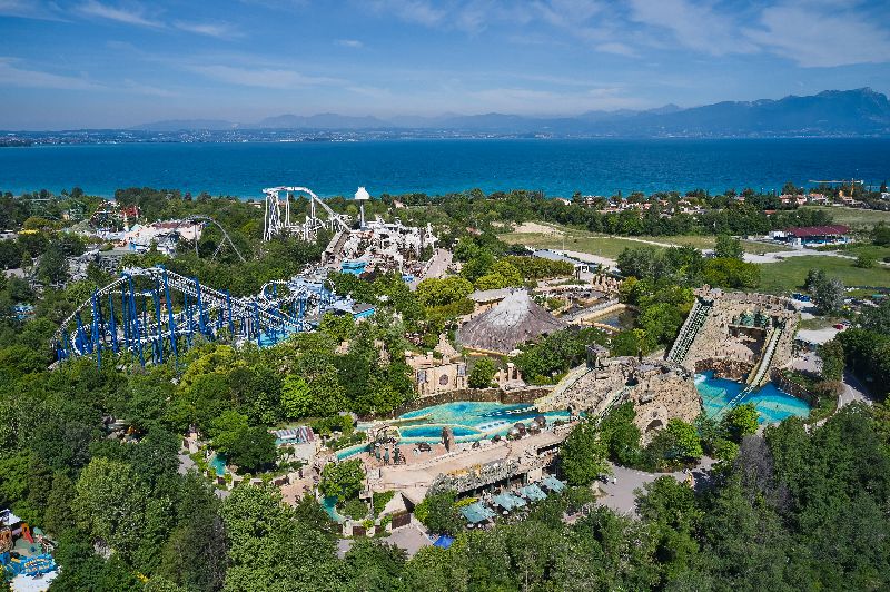 Luftaufnahme des Gardaland Freizeitparks mit Achterbahnen und Wasserattraktionen vor der Kulisse des Gardasees.
