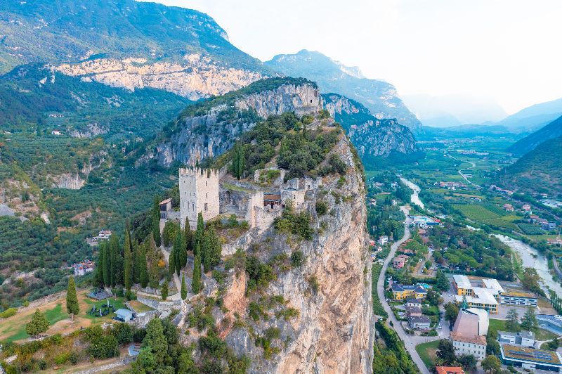 Luftaufnahme der Burgruine Arco auf einem Felsen über dem Sarcatal.