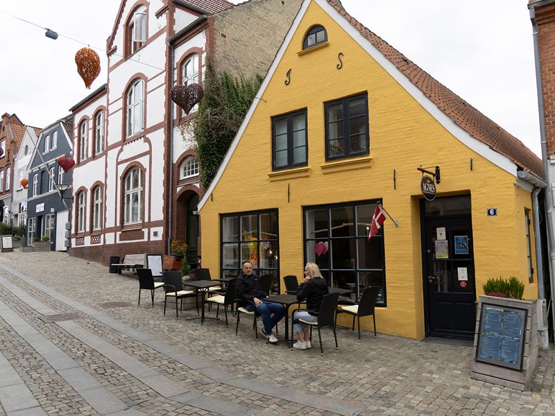 Ricarda und Lars sitzen auf Stühlen vor dem alten, gelben Gebäude des Cafés in Aabenraa