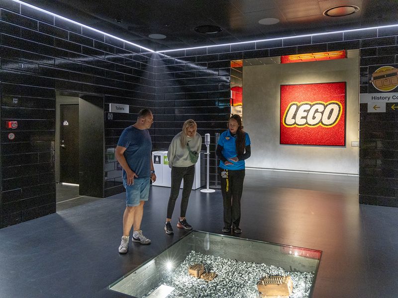 Ricarda und Lars bestaune alte Holz LEGO® Steine, mit dem bekannten LEGO® Logo im Hintergrund.