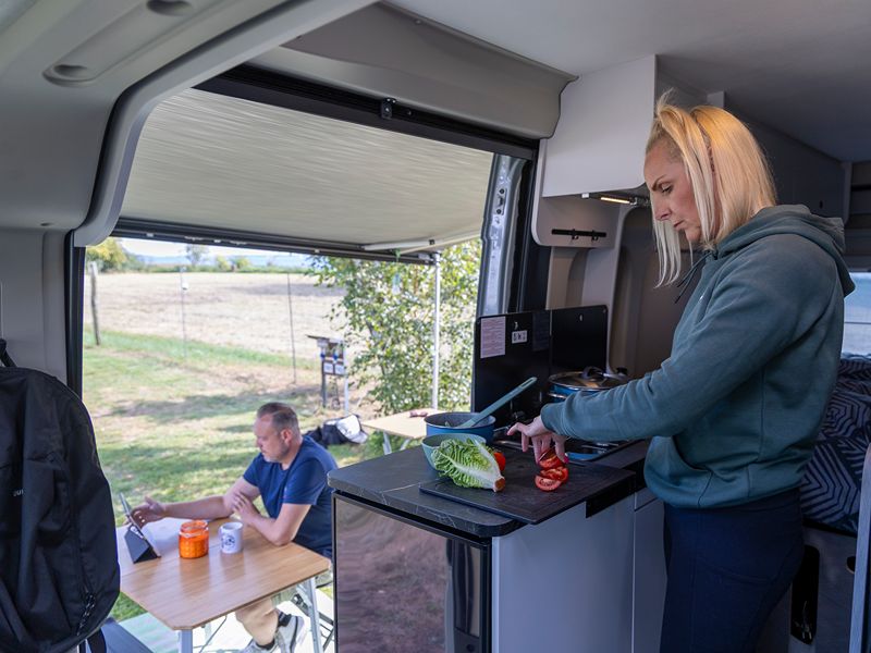 Ricarda bereitet einen Salat zu, Lars sitz außen am Tisch am Ipda