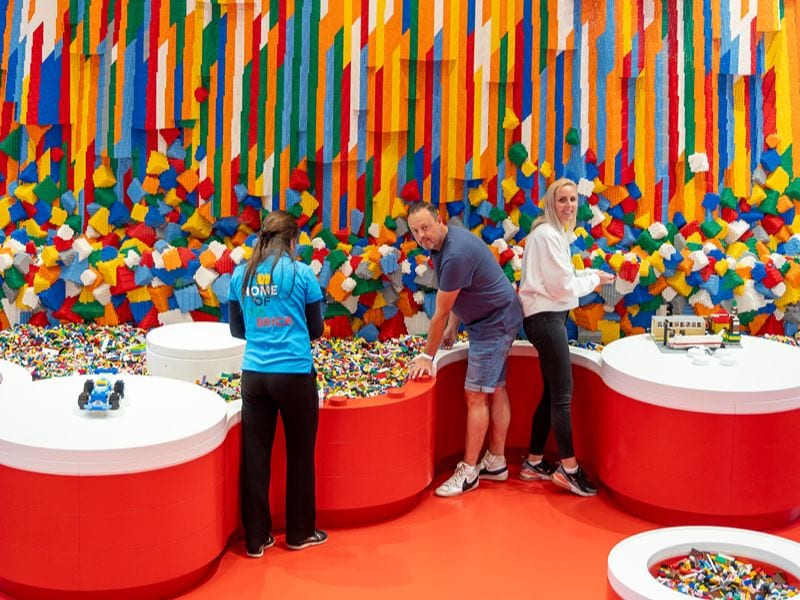 Ricarda und Lars stehen an dem Wasserfall aus LEGO® Steinen und schauen in das Becken voller LEGO® Steine in verschiedensten Farben.