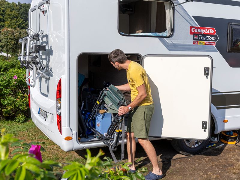 Felix räumt Campingstühle in die Heckgarage des Campers.