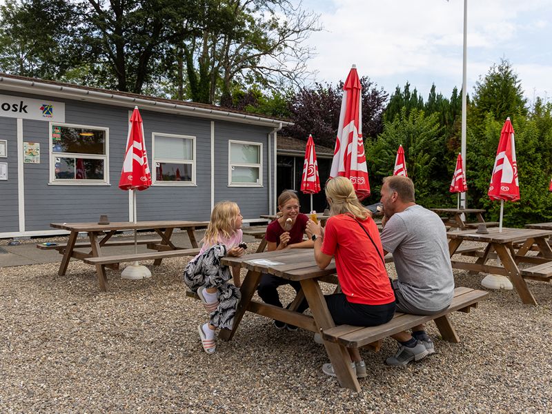 Die vier Rienhoffs sitzen vor der Rezeption des Campingplatzes auf einer Picknickbank und essen jeder eine Eis.