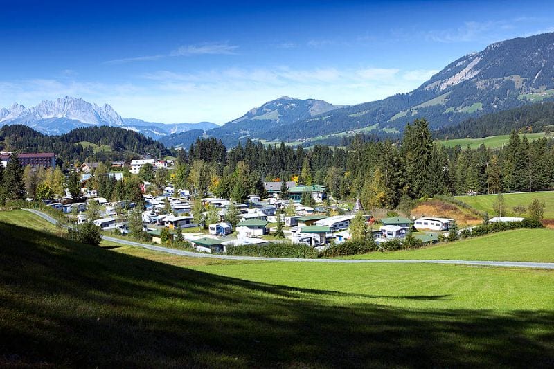 Übersicht über das Tirol Camp in einem grünen Tal mit Wohnwagen und Wohnmobilen, umgeben von Bergen und Wäldern in Österreich