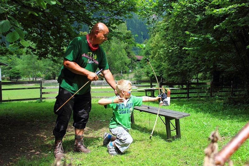 Ein Mann hilft einem Kind beim Bogenschießen auf einem grünen Campingplatz beim Komfort-Campingpark Burgstaller in Österreich