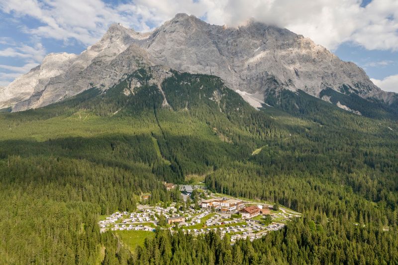 Luftaufnahme des Zugspitz Resort Camping am Fuße eines imposanten Berges, umgeben von dichtem Wald in Österreich