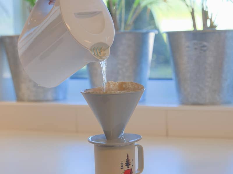 Wasserkocher, der Wasser in einen Kaffeefilter auf einer Tasse gießt