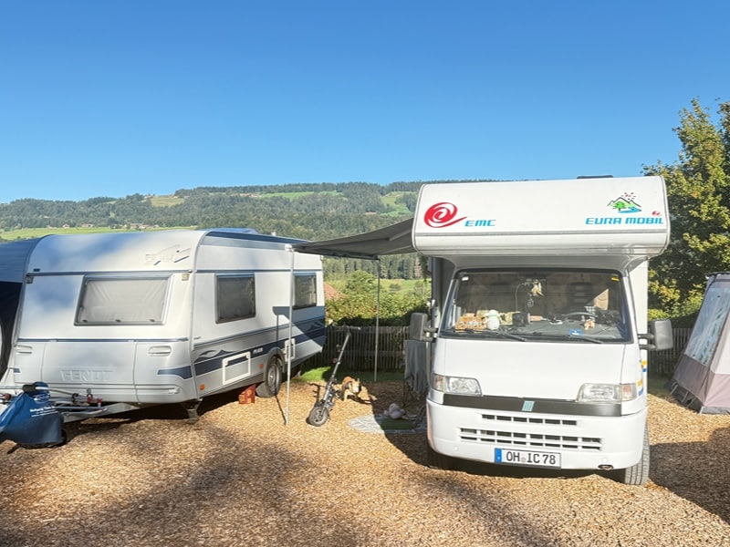 Camper in mitten der bayrischen Natur: Weißer Camper mit Vordach steht neben Caravan vor der bergigen Kulisse