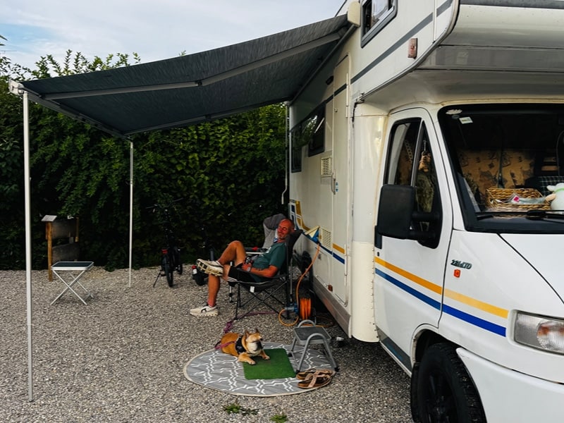 Sven und Hündin Bärbel sitzen bzw. liegen vor dem Camper unter dem Vordach